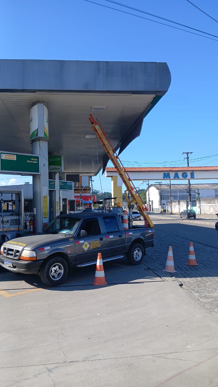 Serviço de manutenção elétrica na cobertura de um posto de combustível com escada apoiada e caminhonete da Nerel Elétrica
